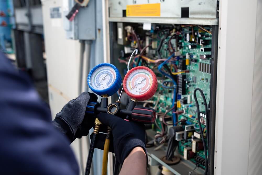 An HVAC technician wearing gloves using a gauge to check the refrigerant in an AC unit
